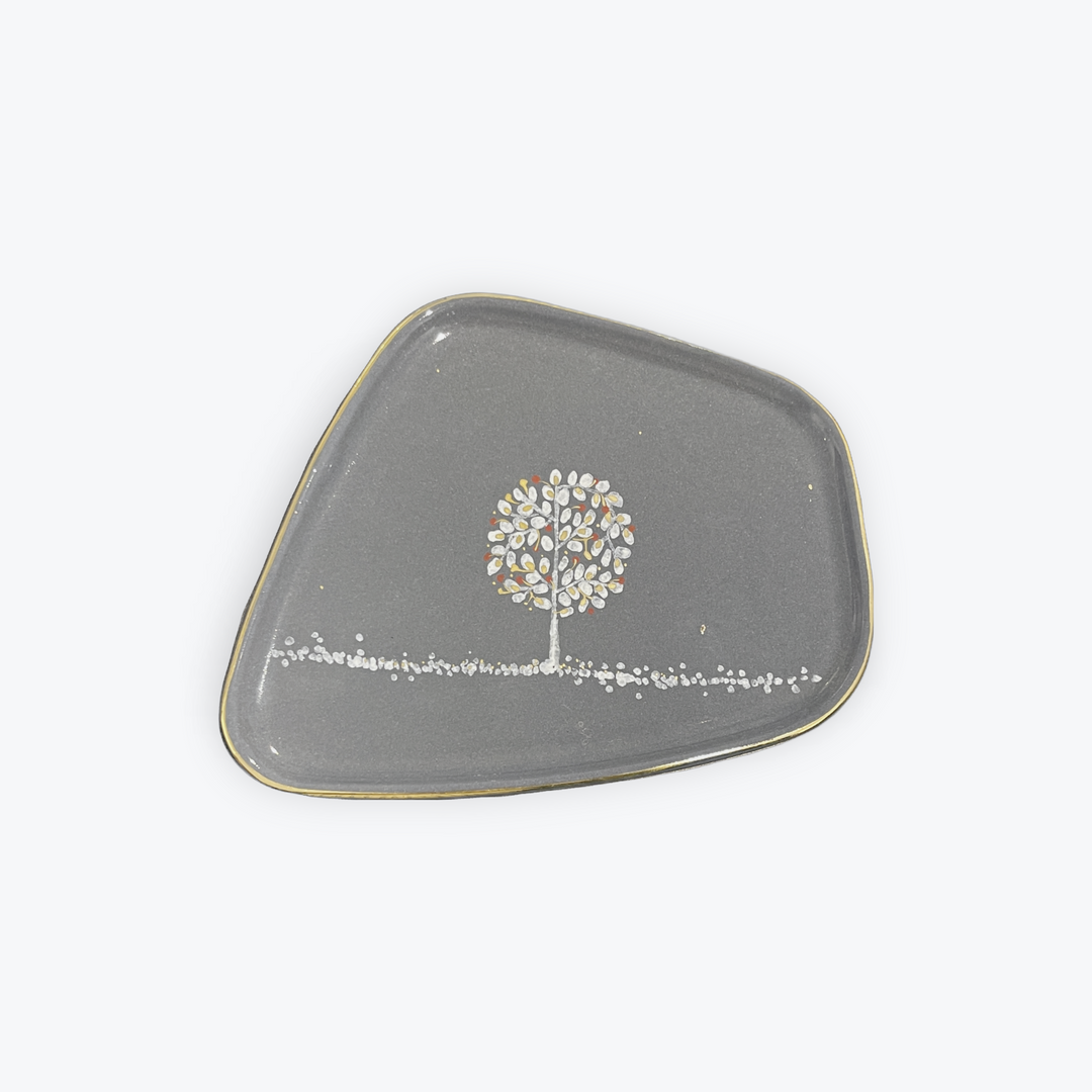 A gray ceramic tray with an organic, rounded triangular shape, featuring a small white and gold tree design in the center and a gold rim, shown on a plain white background.