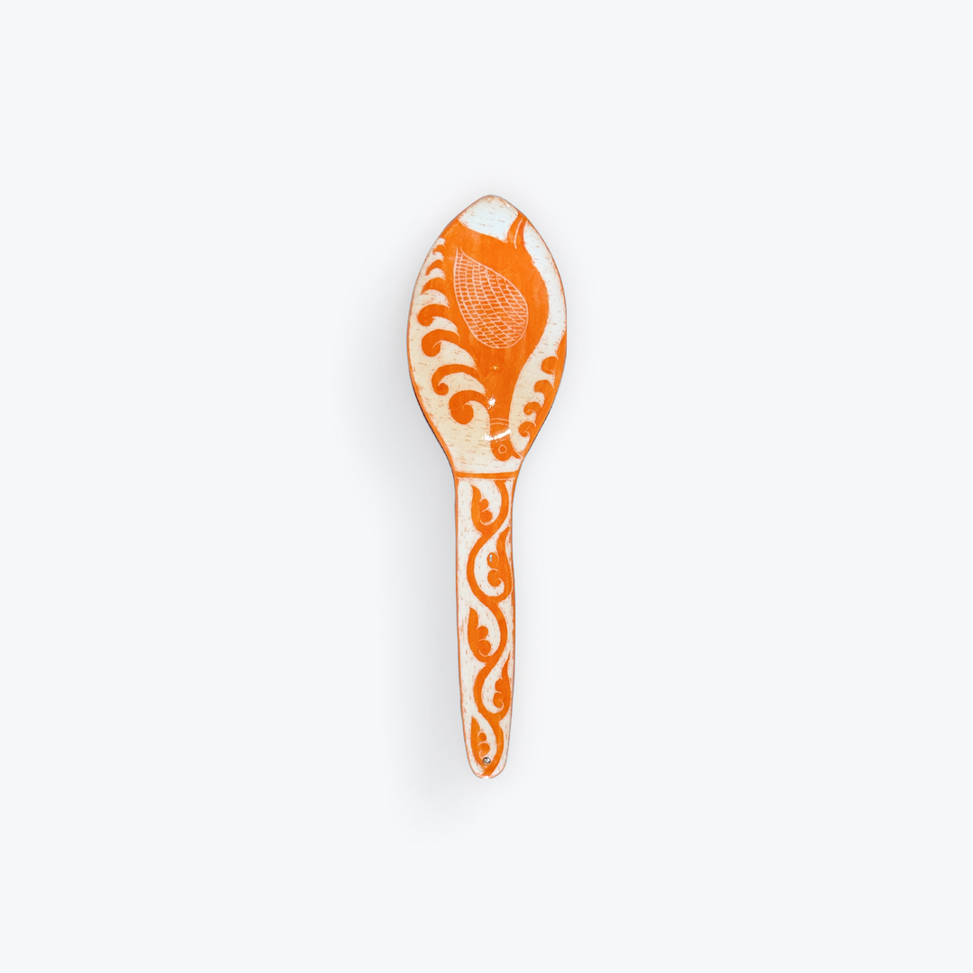 An orange and white decorative spoon with intricate hand-painted floral and scroll patterns, shown against a plain light gray background.