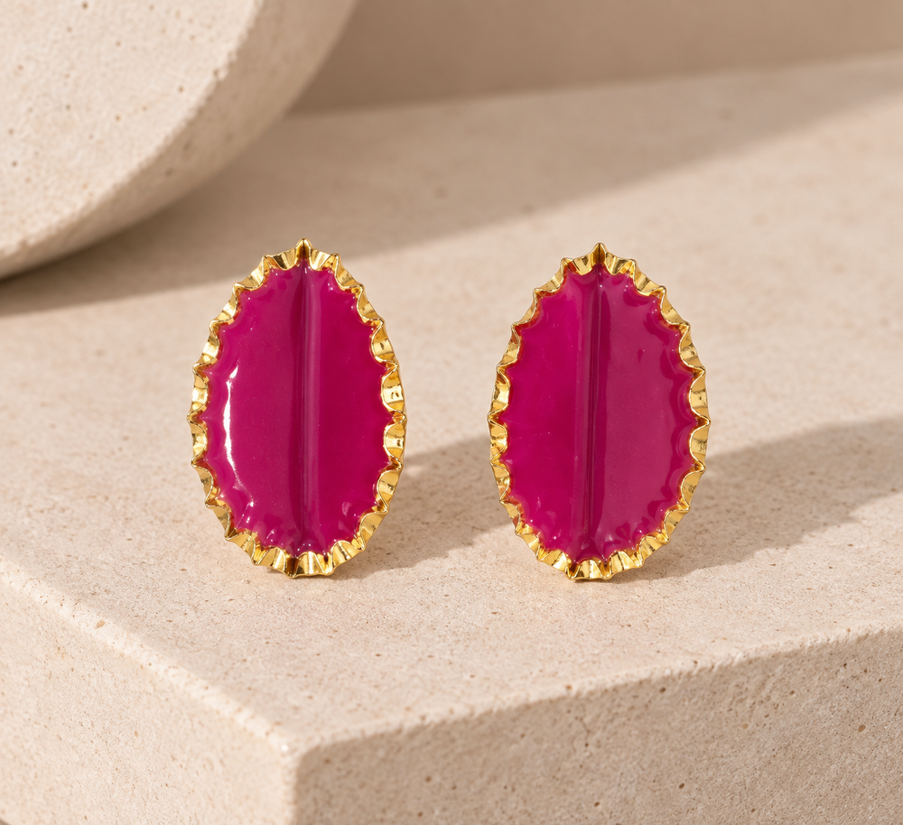 Tashtak fuchsia statement earrings with sculptural gold-toned edges displayed on a neutral stone surface.