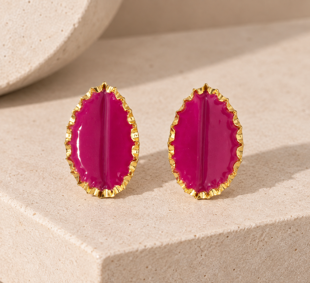 Tashtak fuchsia statement earrings with sculptural gold-toned edges displayed on a neutral stone surface.