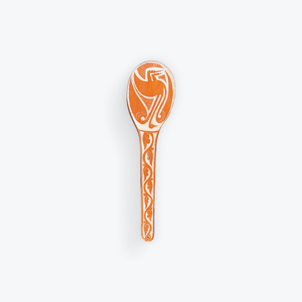 An orange and white decorative spoon with a stylized bird design on the bowl and a patterned handle, shown against a plain light gray background.