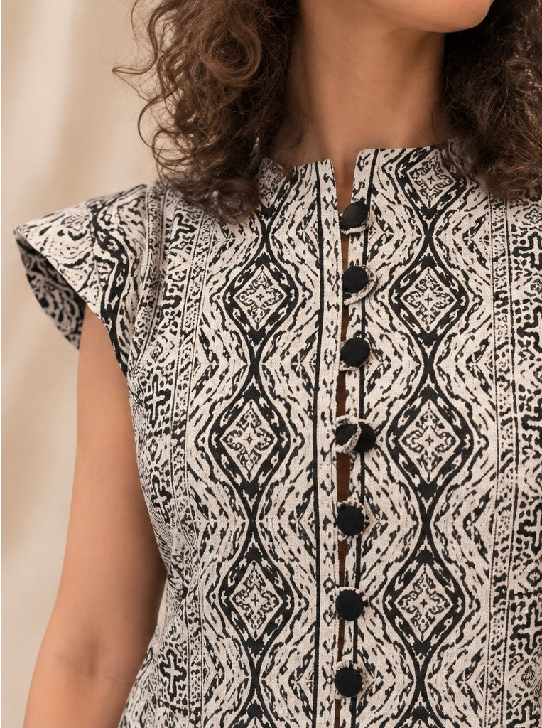 Close-up of black and ivory patterned dress showing structured shoulders, neckline and fabric-covered button details