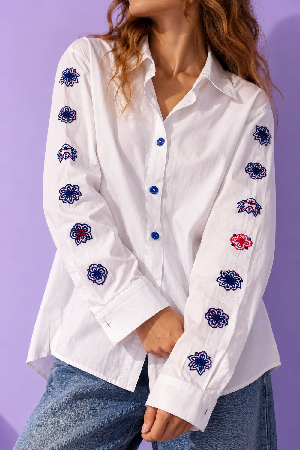 Close-up of ZAAK white button-up shirt featuring hand-embroidered navy blue and red floral motifs on both sleeves, signature blue buttons and classic shirt collar.