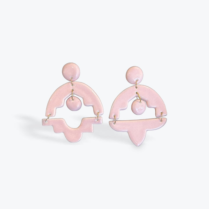 A pair of light pink geometric statement earrings with gold-tone wire accents, displayed against a clean, light gray background.