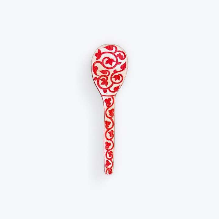 A single decorative spoon with a red and white floral scroll pattern, shown against a plain light gray background.