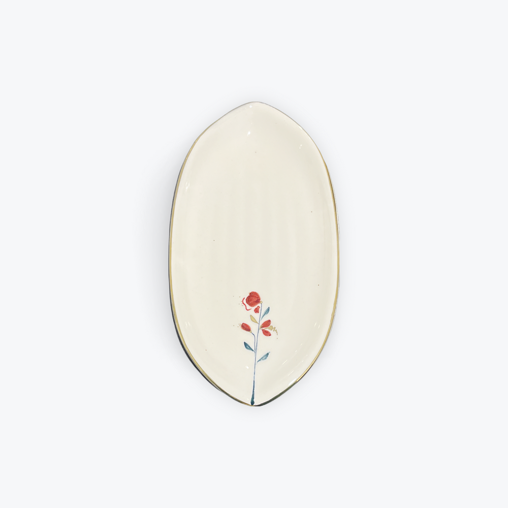 An oval ceramic dish with a cream-colored glaze, featuring a small painted red flower with green and orange details near the bottom center, and a thin dark rim.