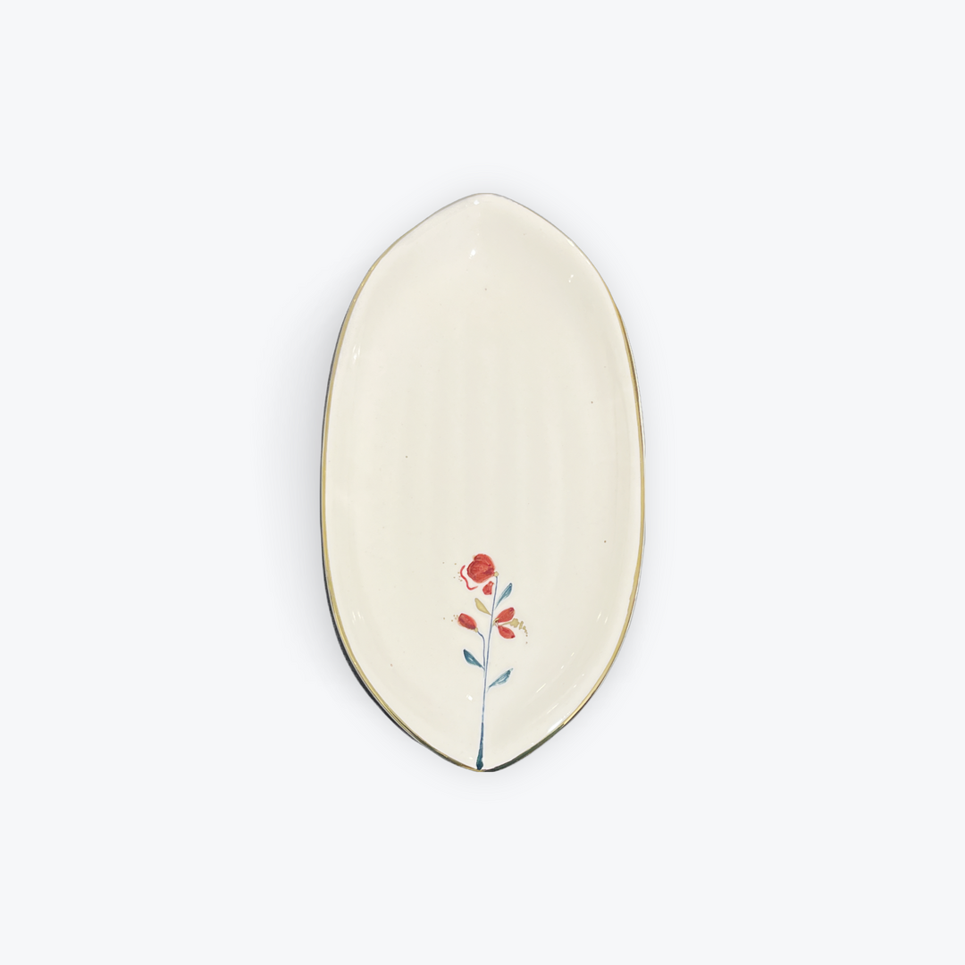 An oval ceramic dish with a cream-colored glaze, featuring a small painted red flower with green and orange details near the bottom center, and a thin dark rim.