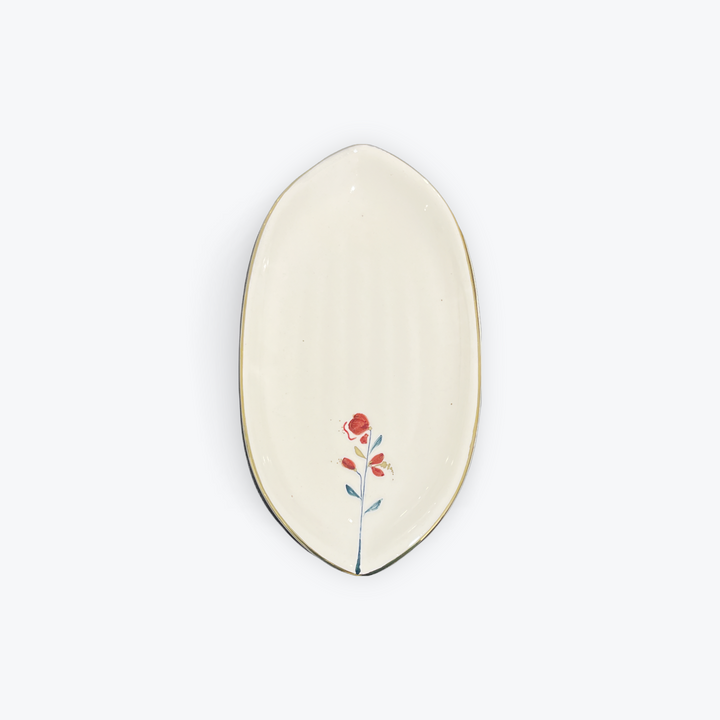 An oval ceramic dish with a cream-colored glaze, featuring a small painted red flower with green and orange details near the bottom center, and a thin dark rim.