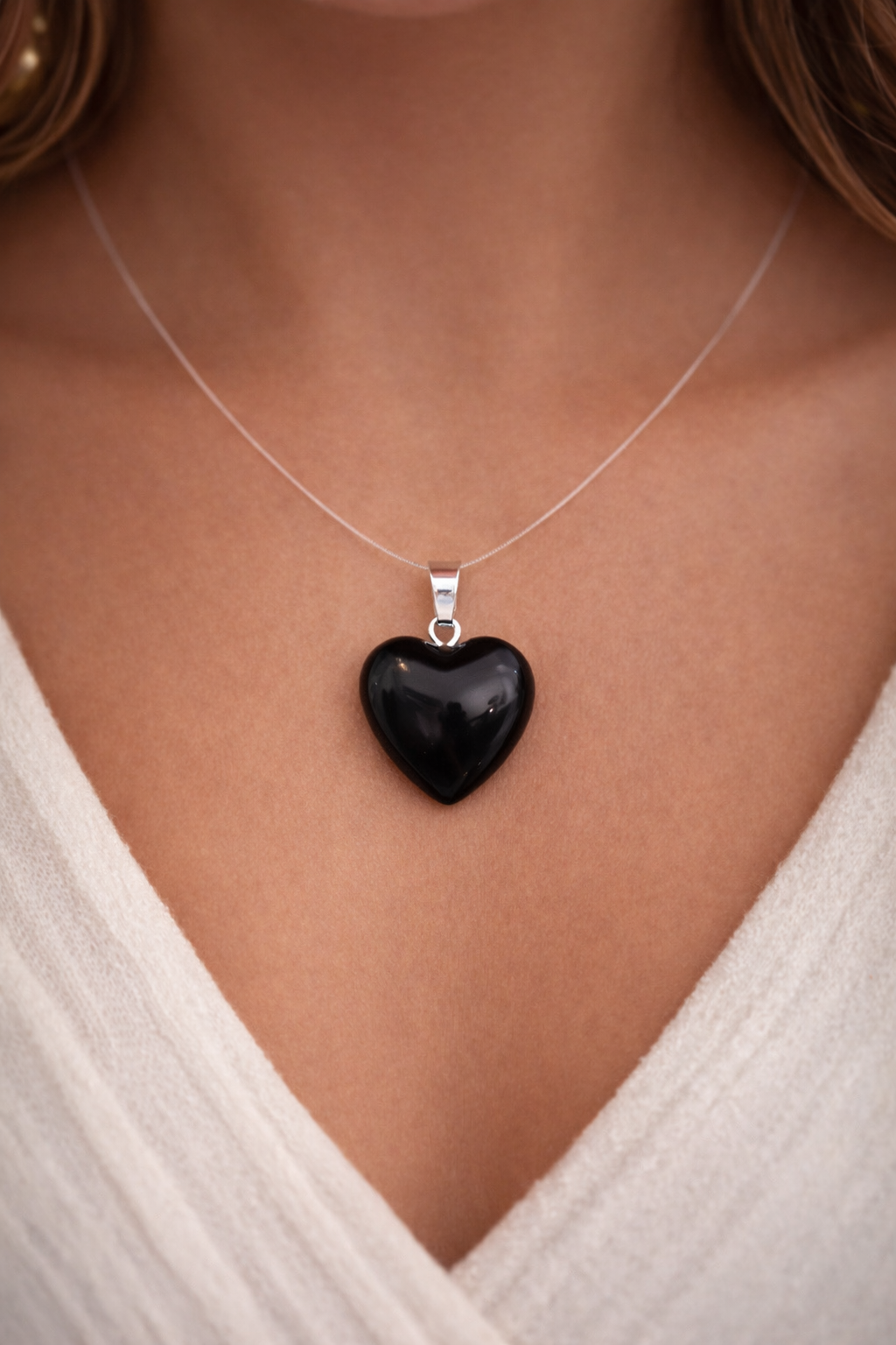 Black heart-shaped pendant on a silver necklace worn by a person in a white top.