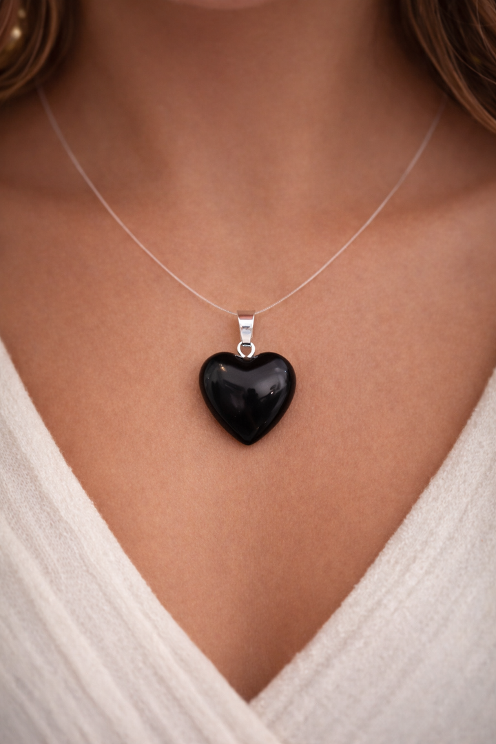 Black heart-shaped pendant on a silver necklace worn by a person in a white top.