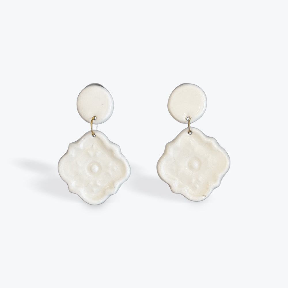 A pair of white resin drop earrings with a circular stud and a textured, flower-like dangle, shown on a light gray background.
