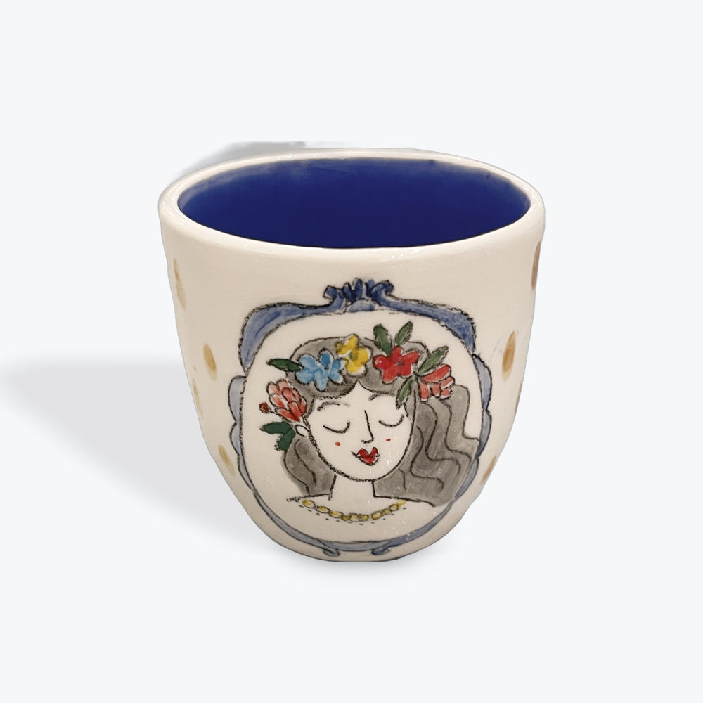 Ceramic cup with a decorative design of a face with flowers on a white background