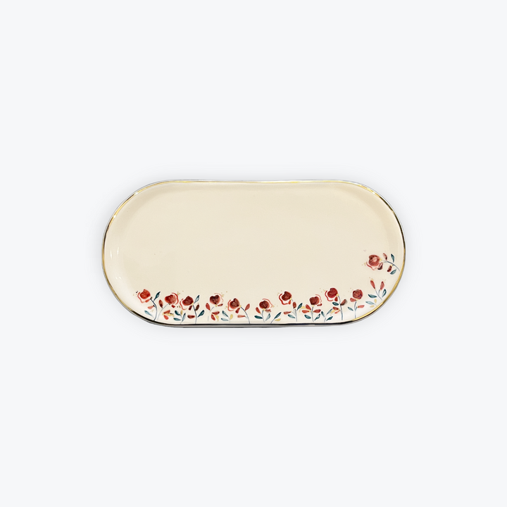 An oval cream-colored ceramic serving tray with a delicate border of red flowers and green leaves along the bottom edge, set against a plain light gray background.