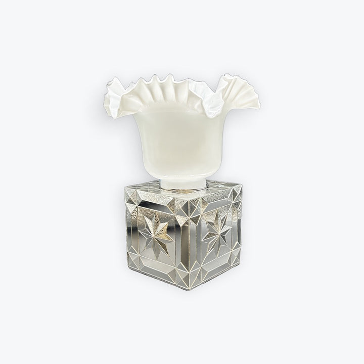 A vintage-style perfume bottle featuring a faceted, star-cut clear glass base and a white ruffled glass neck, set against a plain light gray background.