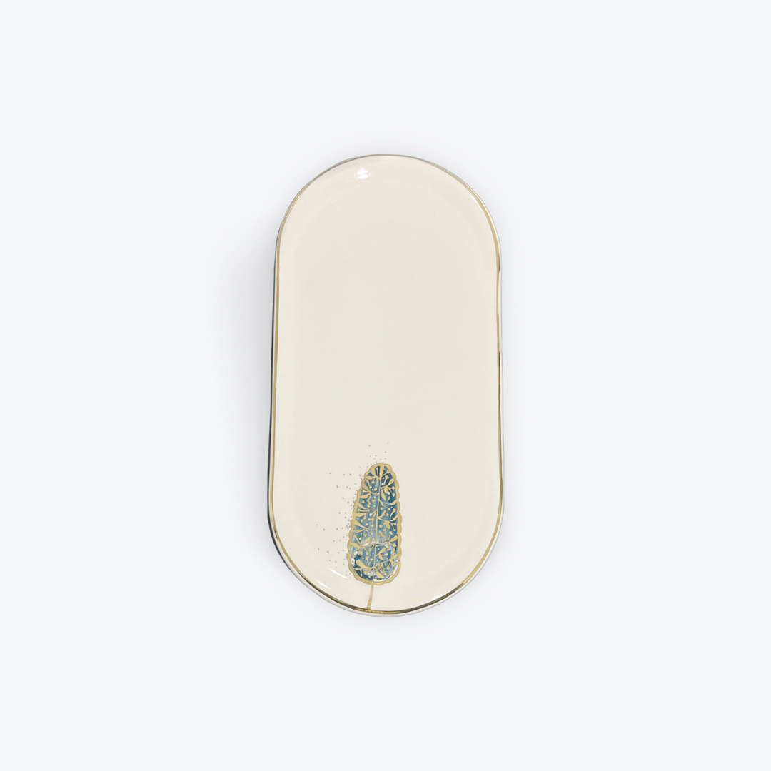 An oval cream-colored ceramic dish with a gold-toned rim and a small blue and gold floral accent near the bottom center, shown on a plain white background.