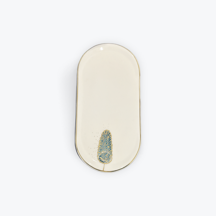 An oval cream-colored ceramic dish with a gold-toned rim and a small blue and gold floral accent near the bottom center, shown on a plain white background.
