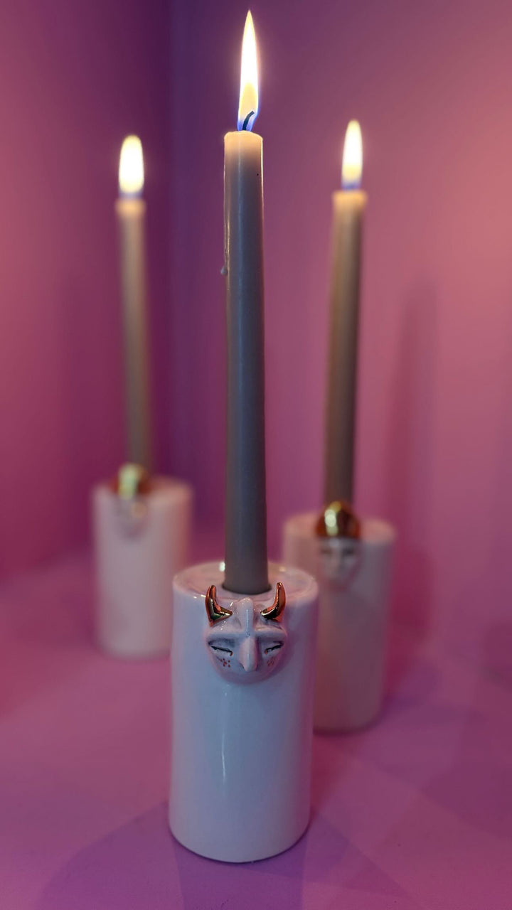 Candle holder with a decorative face design on a pink background