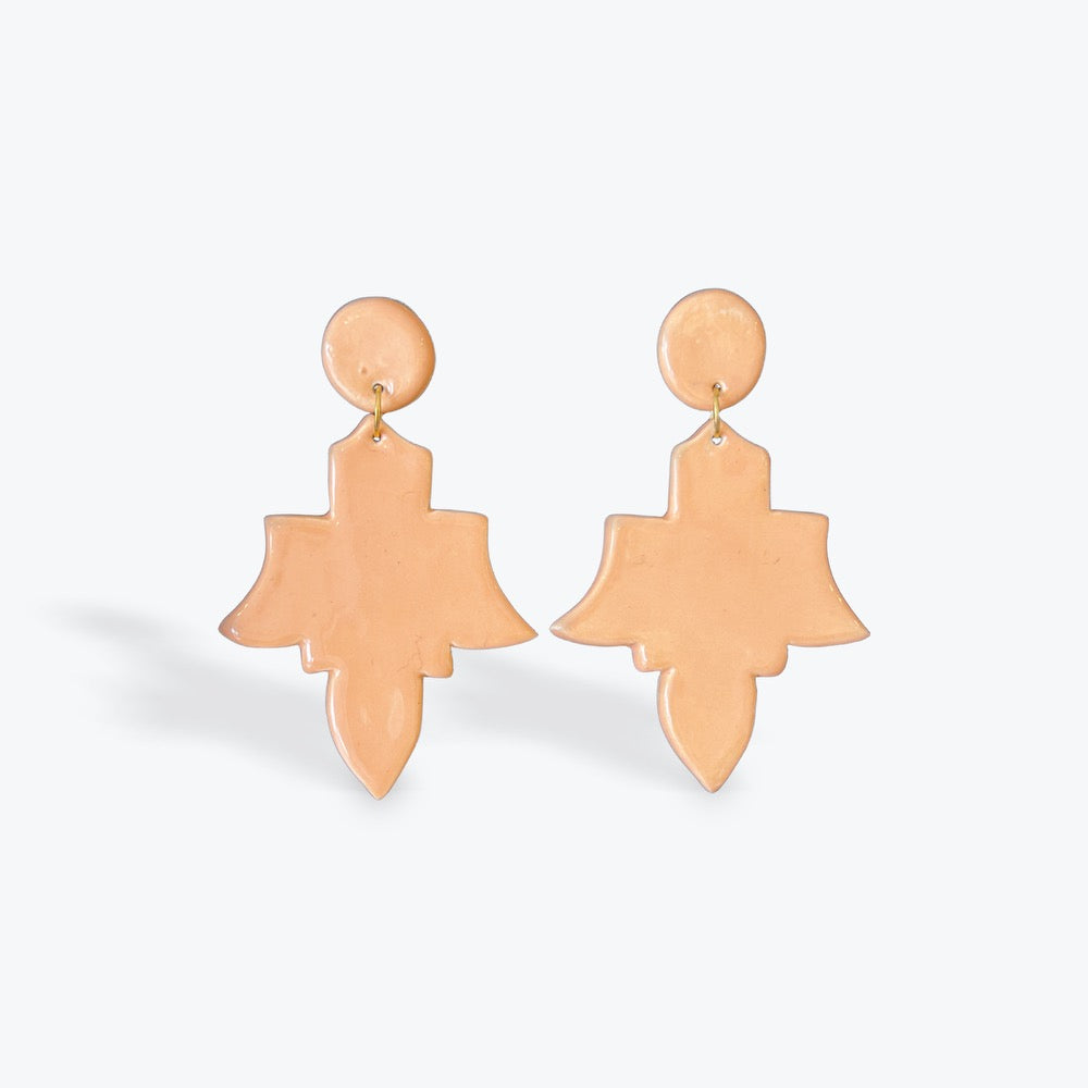 A pair of peach-colored statement earrings with a circular stud and a larger abstract, layered teardrop-shaped drop, shown on a light gray background.