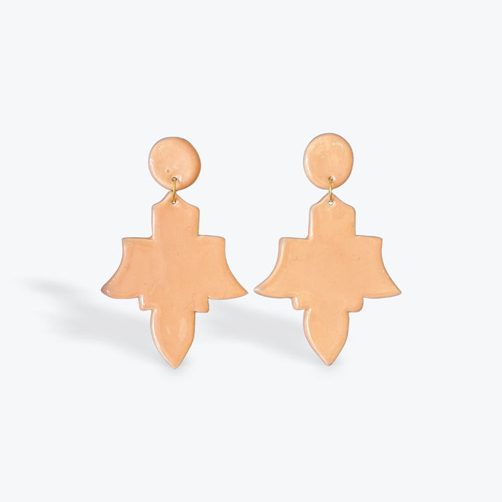 A pair of peach-colored statement earrings with a circular stud and a larger abstract, layered teardrop-shaped drop, shown on a light gray background.