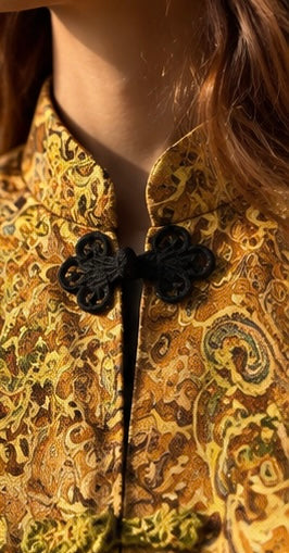 Close-up of a person wearing a patterned yellow and brown traditional-style jacket with black decorative front closures.