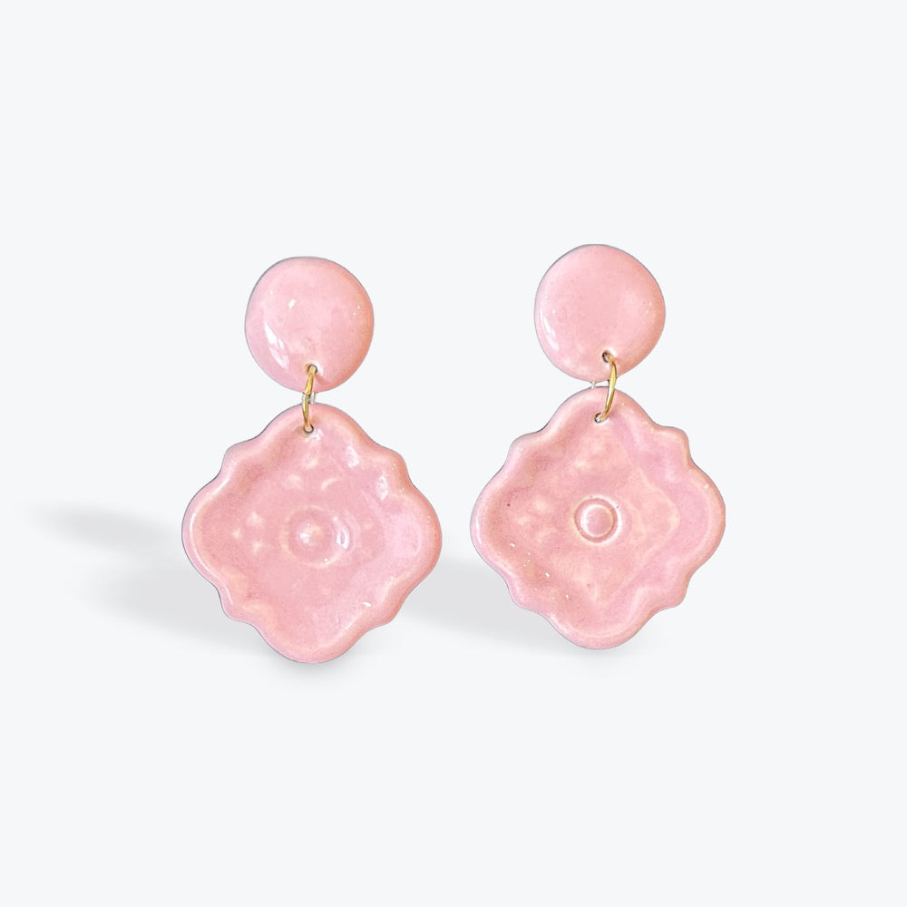 A pair of light pink dangling earrings with round studs and textured, flower-like drop charms, shown on a clean white background.