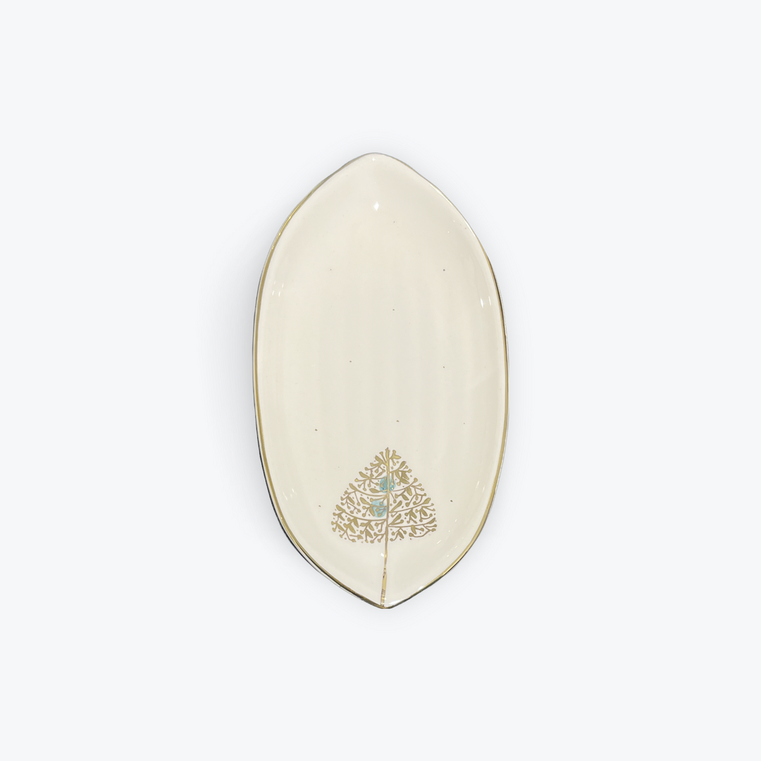 An off-white ceramic oval dish with a gold-trimmed edge and a gold tree design decorated with a small light blue center, shown on a light gray background.