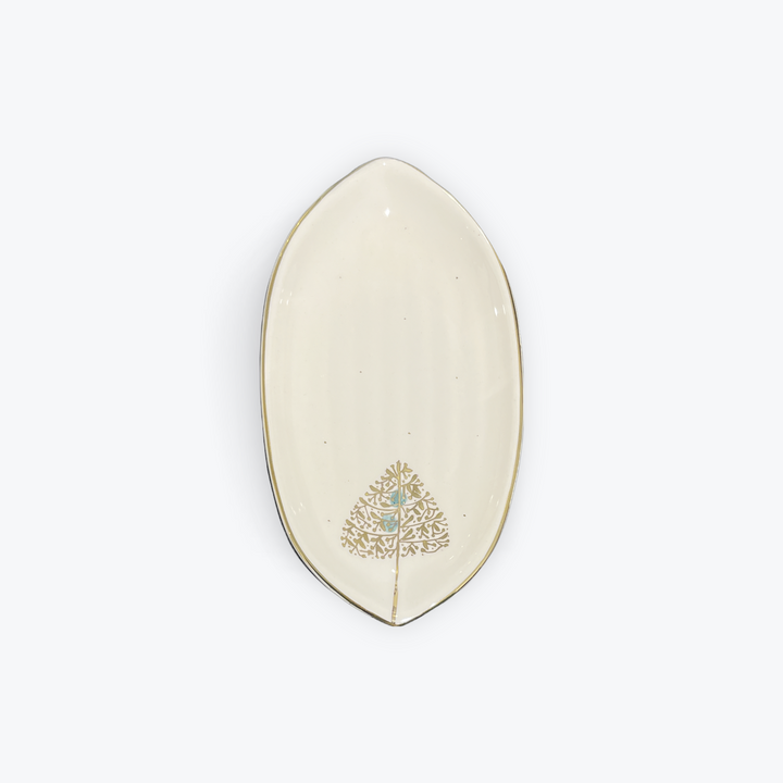 An off-white ceramic oval dish with a gold-trimmed edge and a gold tree design decorated with a small light blue center, shown on a light gray background.