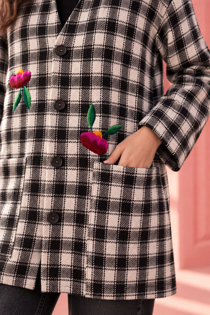 Close-up of black and ivory plaid jacket featuring colorful hand-embroidered flowers, button-front closure and patch pocket.