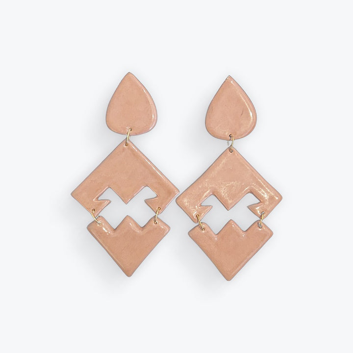 A pair of geometric drop earrings in a glossy peach-pink color, featuring a teardrop-shaped top piece and a larger diamond-shaped lower piece with a zigzag cutout detail, shown on a light gray background.