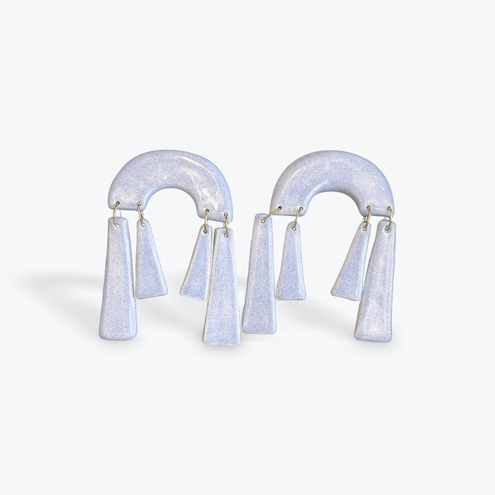 A pair of sculptural arch-shaped earrings with dangling tapered elements, shown on a clean light gray background.