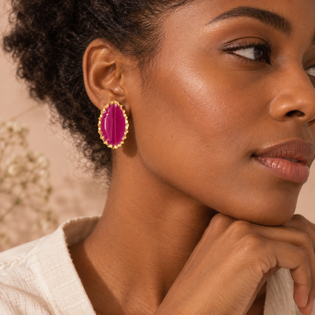 Close-up side portrait of a Black female model wearing a fuchsia Tashtak statement earring with a textured gold-toned edge.
