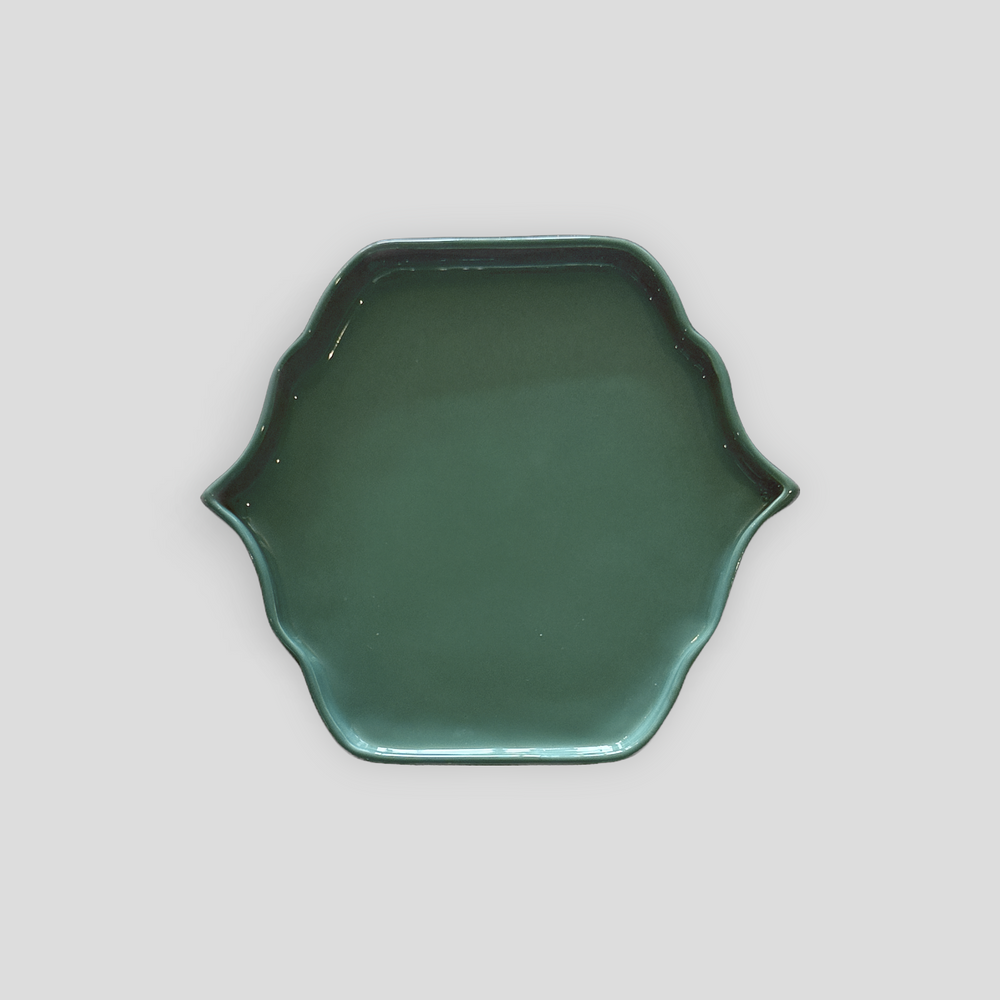 A dark green ceramic plate with a scalloped rim, photographed from directly above on a neutral light gray background.