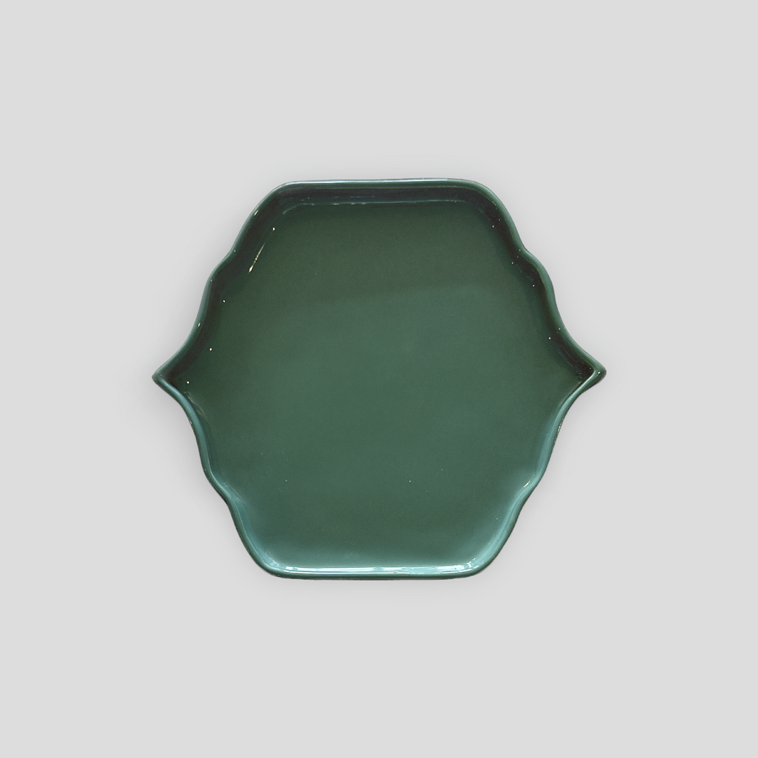 A dark green ceramic plate with a scalloped rim, photographed from directly above on a neutral light gray background.