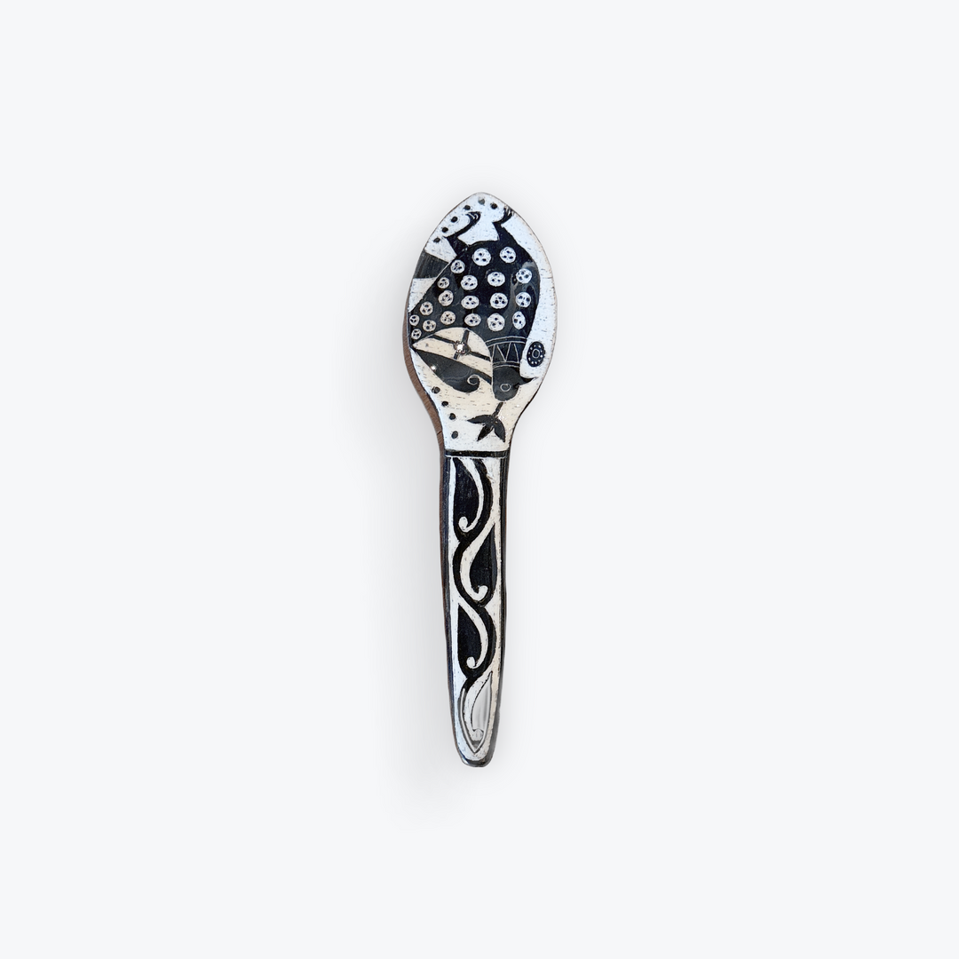 A decorative spoon with a black and white hand-painted pattern, featuring a stylized face on the bowl and flowing lines on the handle, set against a plain white background.