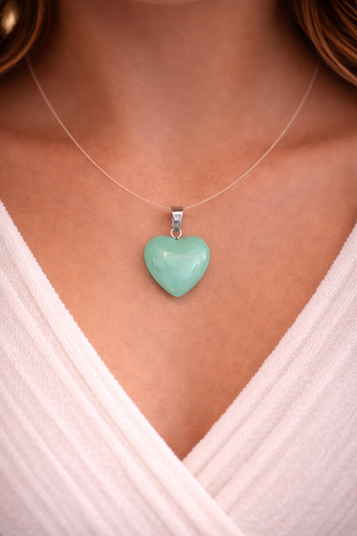 Heart-shaped turquoise pendant on a necklace worn by a person in a white top.
