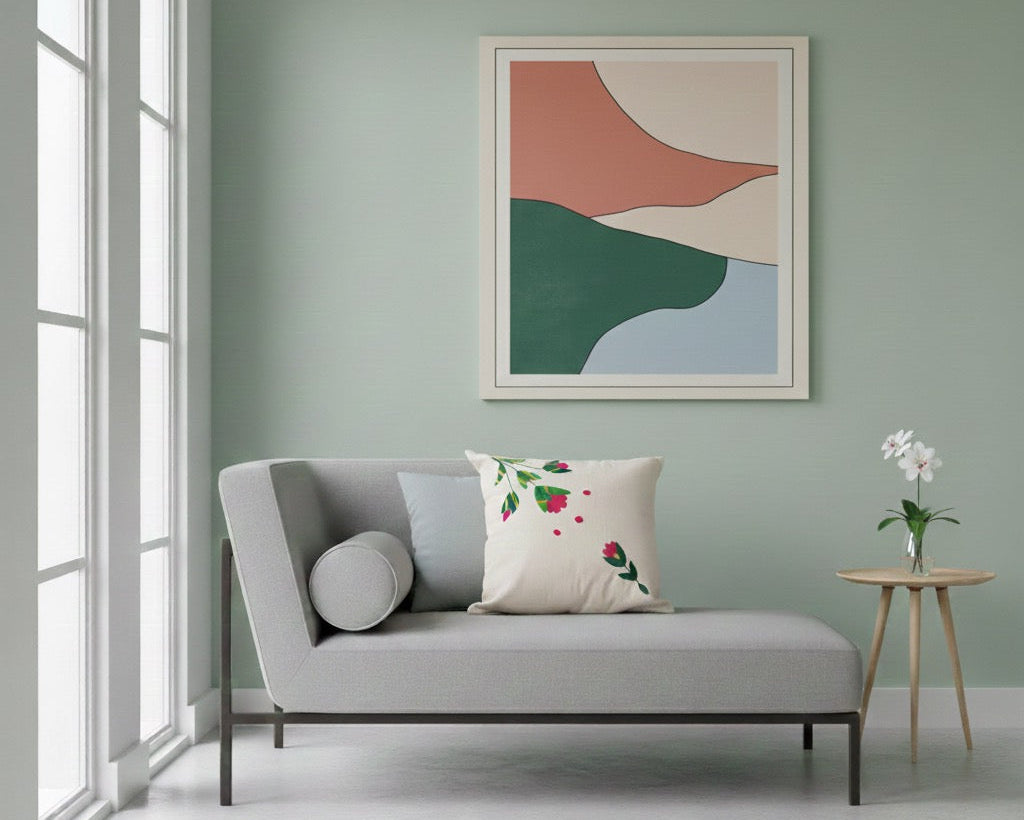 A modern gray chaise lounge with a floral accent pillow, set in a minimalist living room with a sage green wall and an abstract framed art print above.