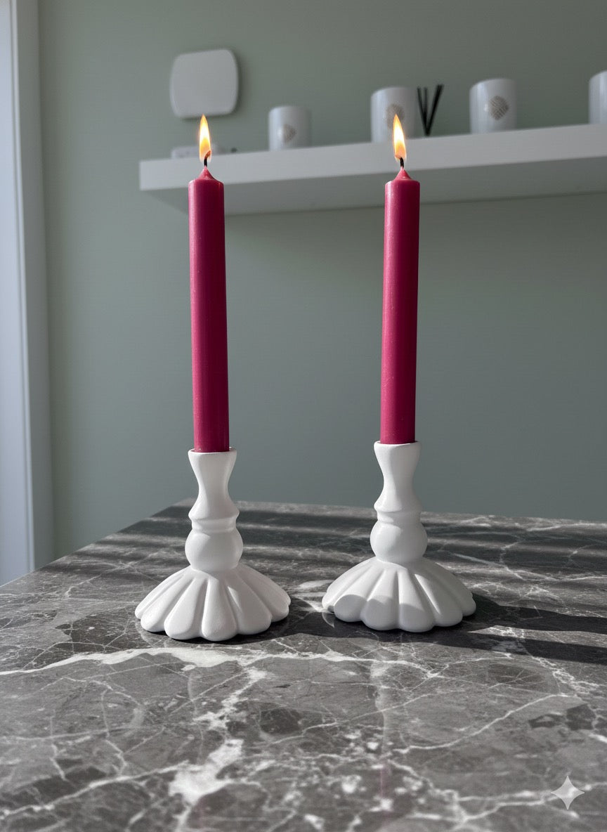 Two white candle holders with red candles on a marble surface.