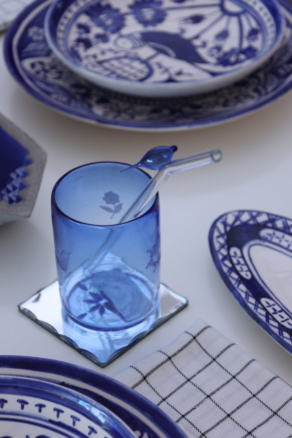 Blue glass with a straw on a white surface with blue and white patterned plates.