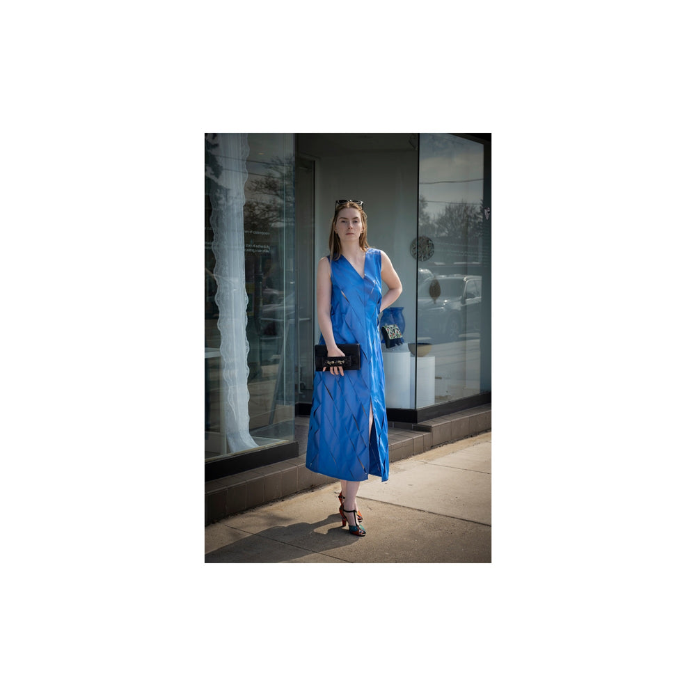 Woman in a blue dress standing on a sidewalk with a store window in the background