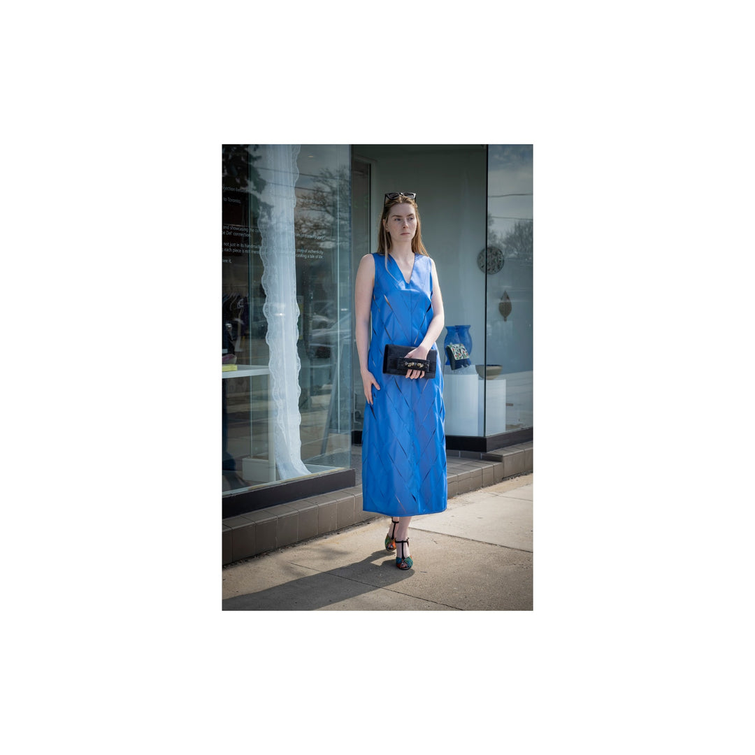 Woman in a blue dress standing on a sidewalk with a store window in the background