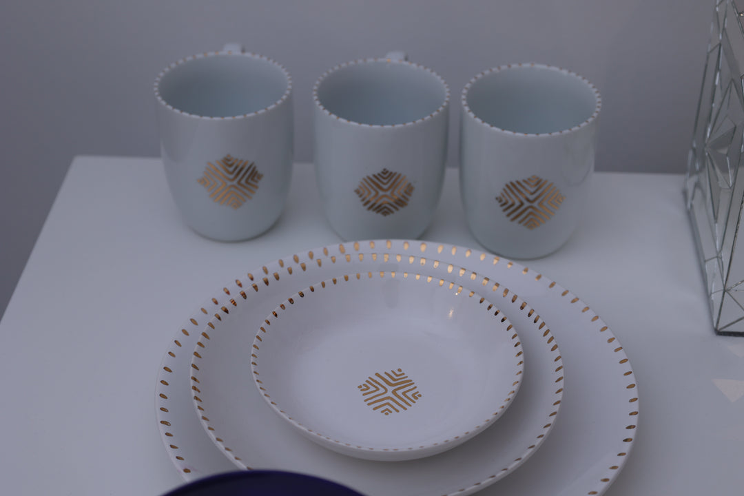 Set of white cups and a plate with gold geometric patterns on a white surface.