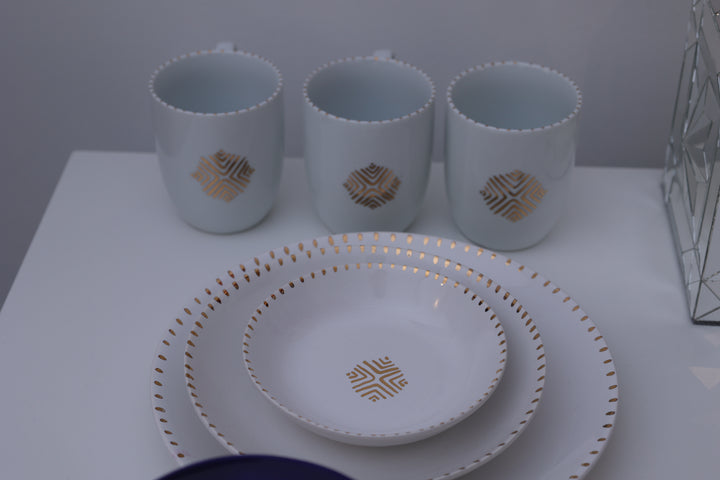 Set of white cups and a plate with gold geometric patterns on a white surface.