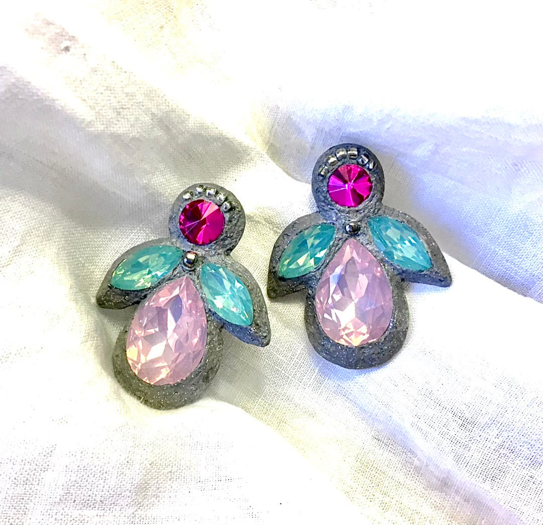 A pair of vintage-style angel wing earrings with faceted pink and light blue rhinestones set in a textured silver-tone metal, displayed on a white fabric background.