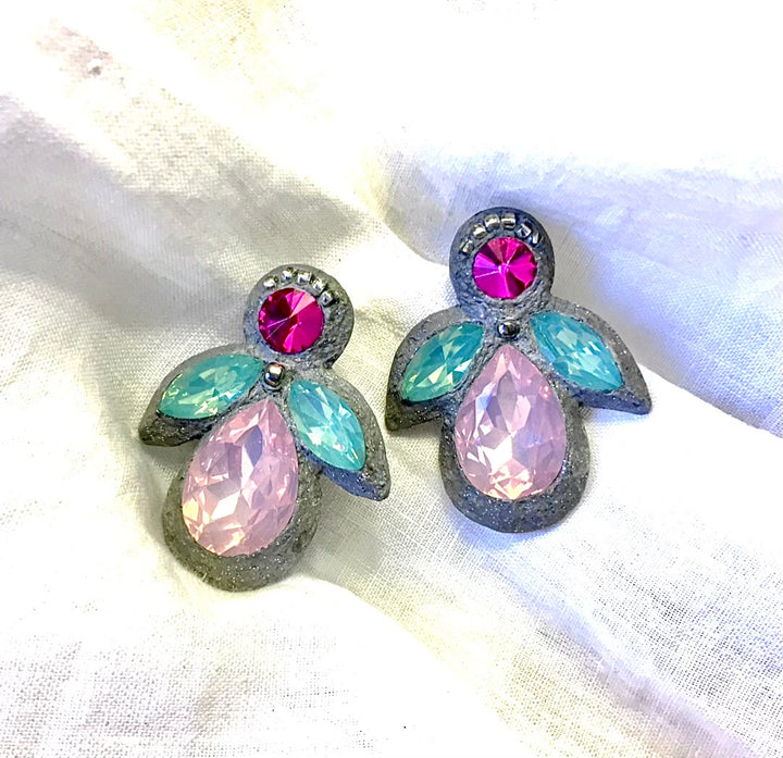 A pair of vintage-style angel wing earrings with faceted pink and light blue rhinestones set in a textured silver-tone metal, displayed on a white fabric background.