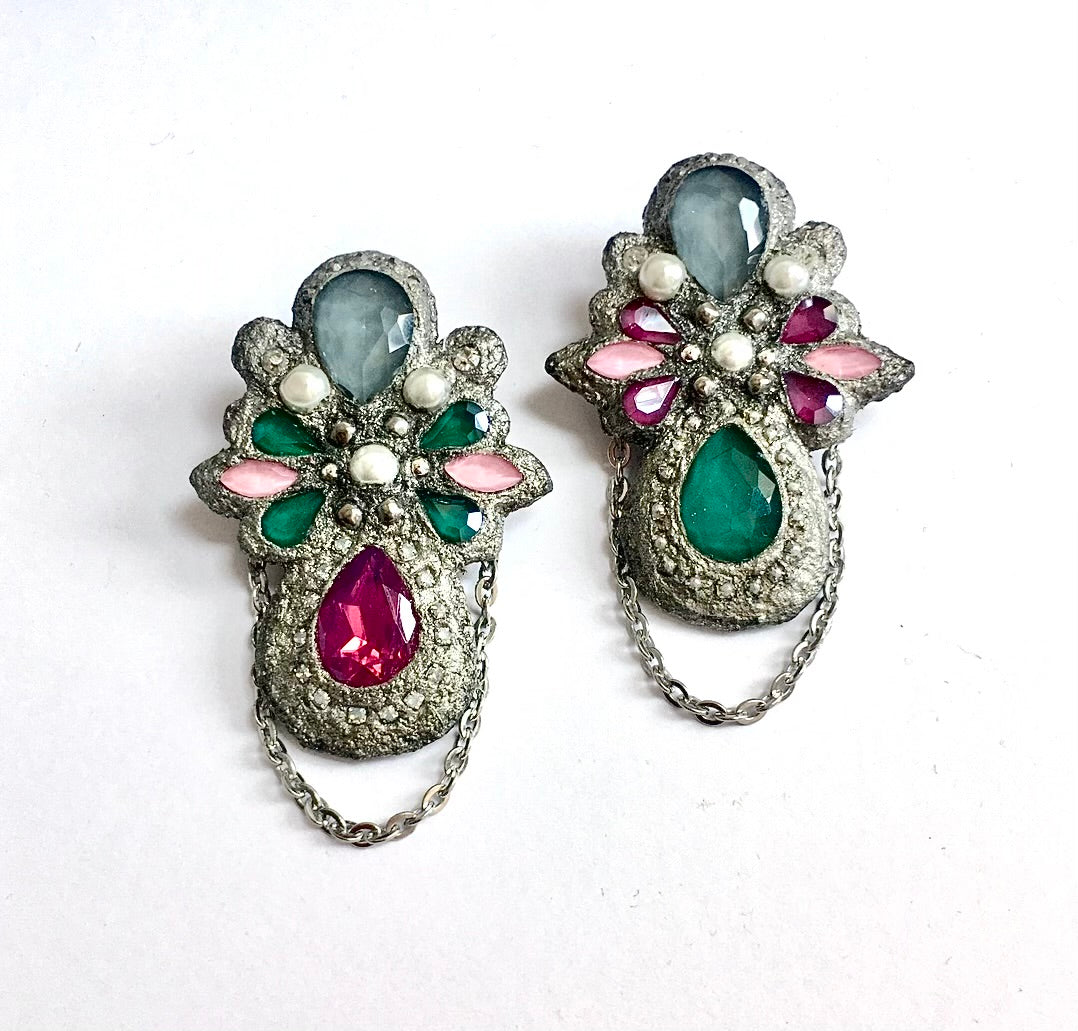 A pair of vintage silver-toned floral brooches decorated with faceted gemstones in green, pink, and gray, with dangling chain accents, displayed on a white background.