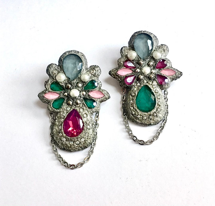 A pair of vintage silver-toned floral brooches decorated with faceted gemstones in green, pink, and gray, with dangling chain accents, displayed on a white background.