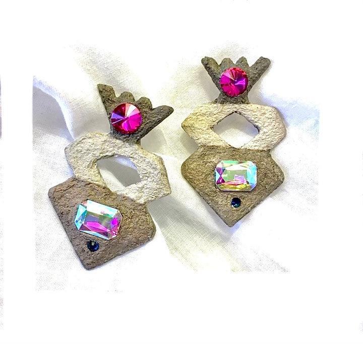 A pair of handmade geometric earrings featuring textured brown and cream stone-like pieces adorned with pink and iridescent rhinestones, set against a white fabric background.