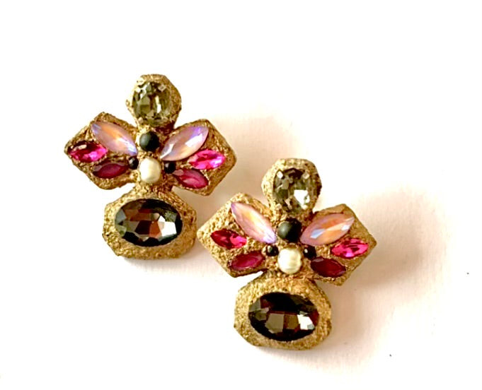 A pair of vintage-style gold-tone stud earrings featuring iridescent pink and purple rhinestones, a small white pearl, and a large faceted dark brown oval stone, set against a plain white background.