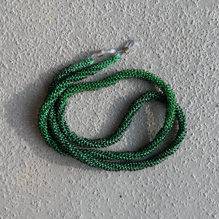 A coiled green braided rope or cord with a clear plastic end cap, placed on a textured gray concrete surface.