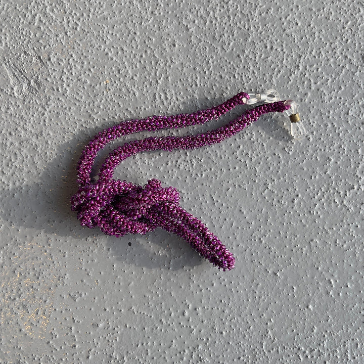 A purple textured rope with a knot and a small white tag, placed on a gray textured concrete surface.
